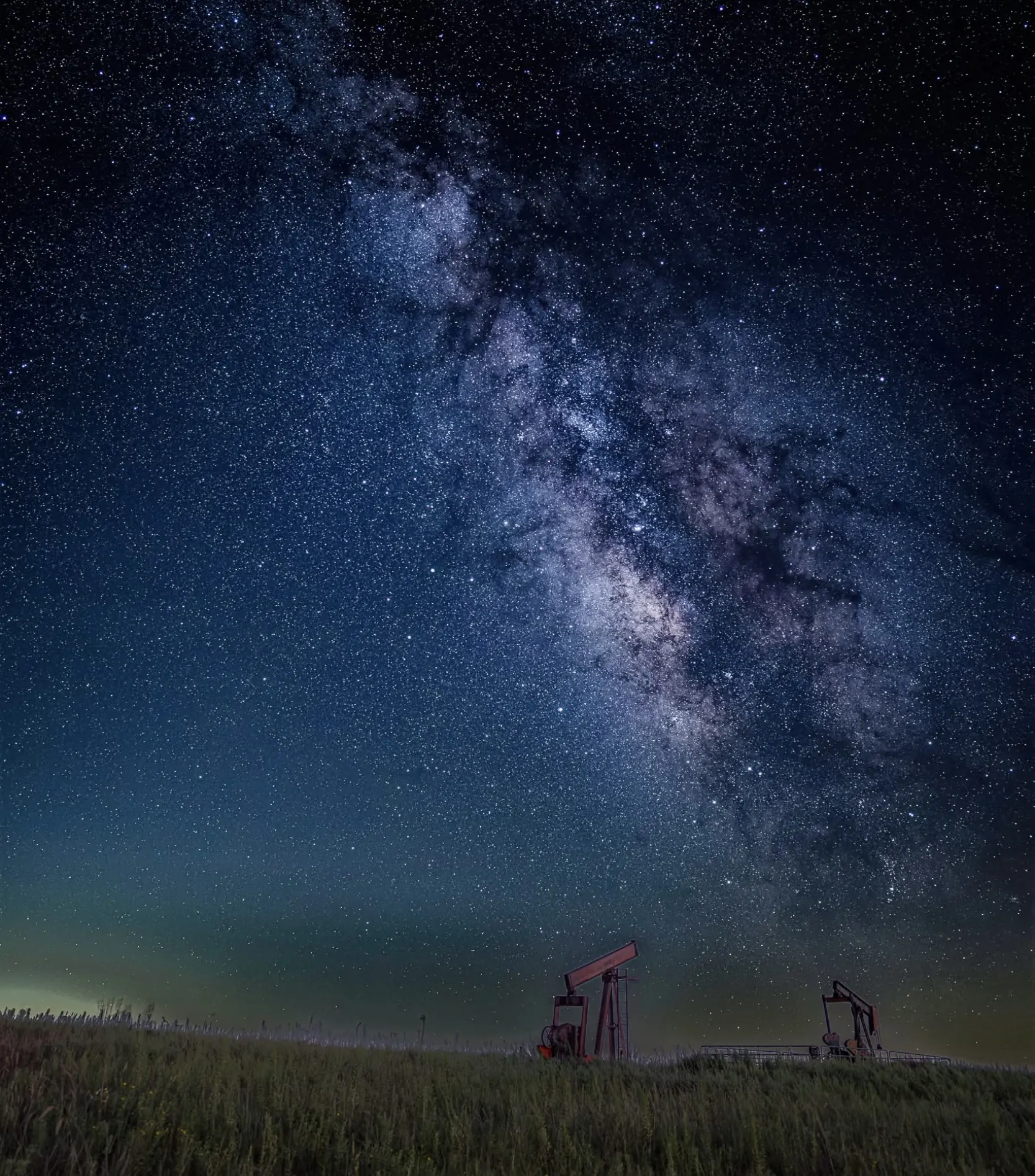 Pumpjacks on rolling grassland under the Milky Way