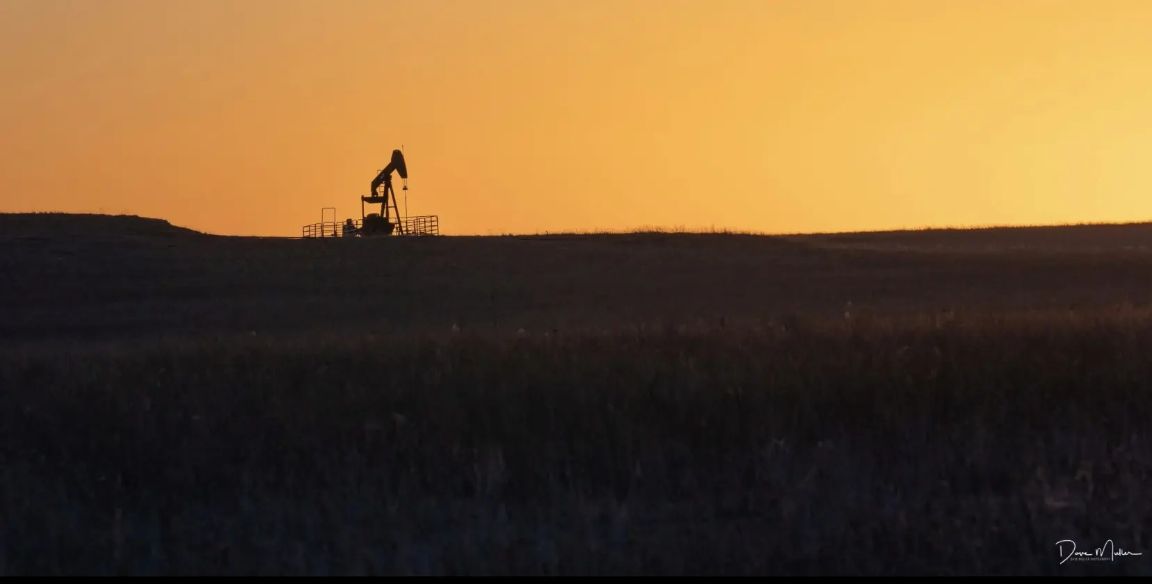Pumpjack silhouetted against an orange prairie sunset